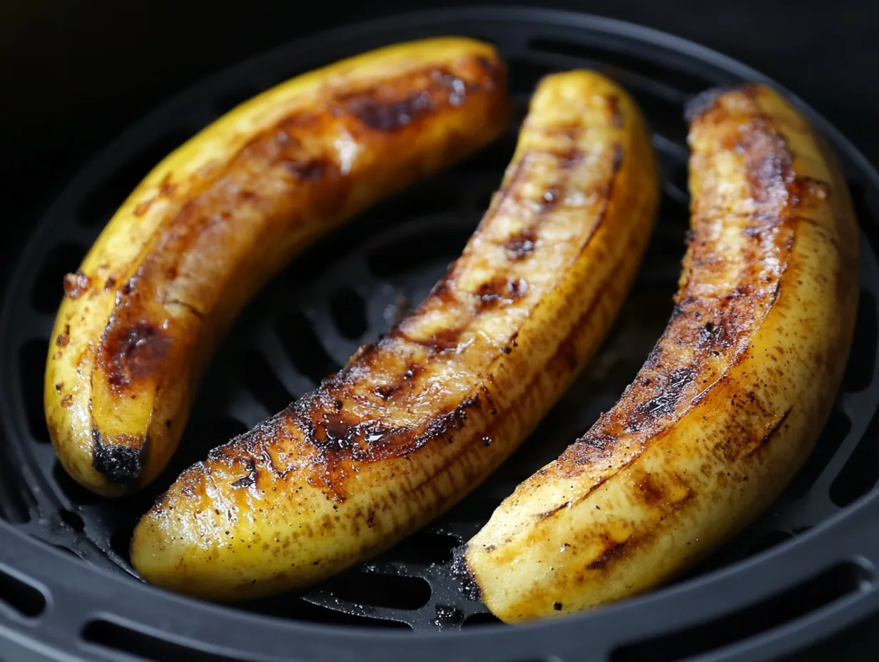 A close-up of golden, caramelized air-fried banana slices served on a white plate with a sprinkle of cinnamon.